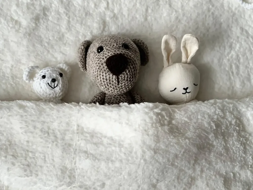 Neutral plush teddy bear and bunny on a soft bed in a cozy nursery setting