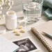 Folic acid supplements beside a glass of water, pregnancy planner, notebook, and ultrasound photo on a softly lit table