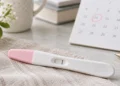 Home pregnancy test on a soft neutral surface beside a calendar, illustrating pregnancy test timing and early testing.